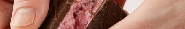The Loada Balls Raspberry Coconuut protein bar split in half by 2 hands showing the pink filling.